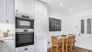 A modern kitchen with white cabinetry, a Bosch oven, a dining table with chairs, and a colorful abstract painting on the wall. - Luxury Modern 5-bed Home Maida Vale (London)