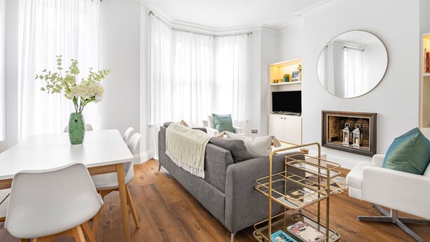 A modern living room with a grey sofa, white chairs, a dining table, and a bookshelf. - Luxury Modern 5-bed Home Maida Vale (London)