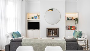 A modern living room with a flat-screen TV, a round mirror, and bookshelves. - Luxury Modern 5-bed Home Maida Vale (London)