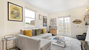 A living room with a sofa, a coffee table with chess pieces, and a bookshelf. - Stylish 1BR Kensington Home With Balcony (London)