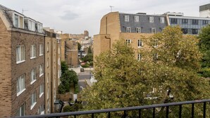 A residential area with brick buildings, a tree in the foreground, and a clear sky. - Stylish 1BR Kensington Home With Balcony (London)