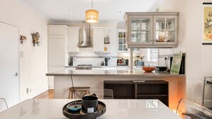 A modern kitchen with white cabinetry, a central island, and a hanging light fixture. - Stylish 1BR Kensington Home With Balcony (London)