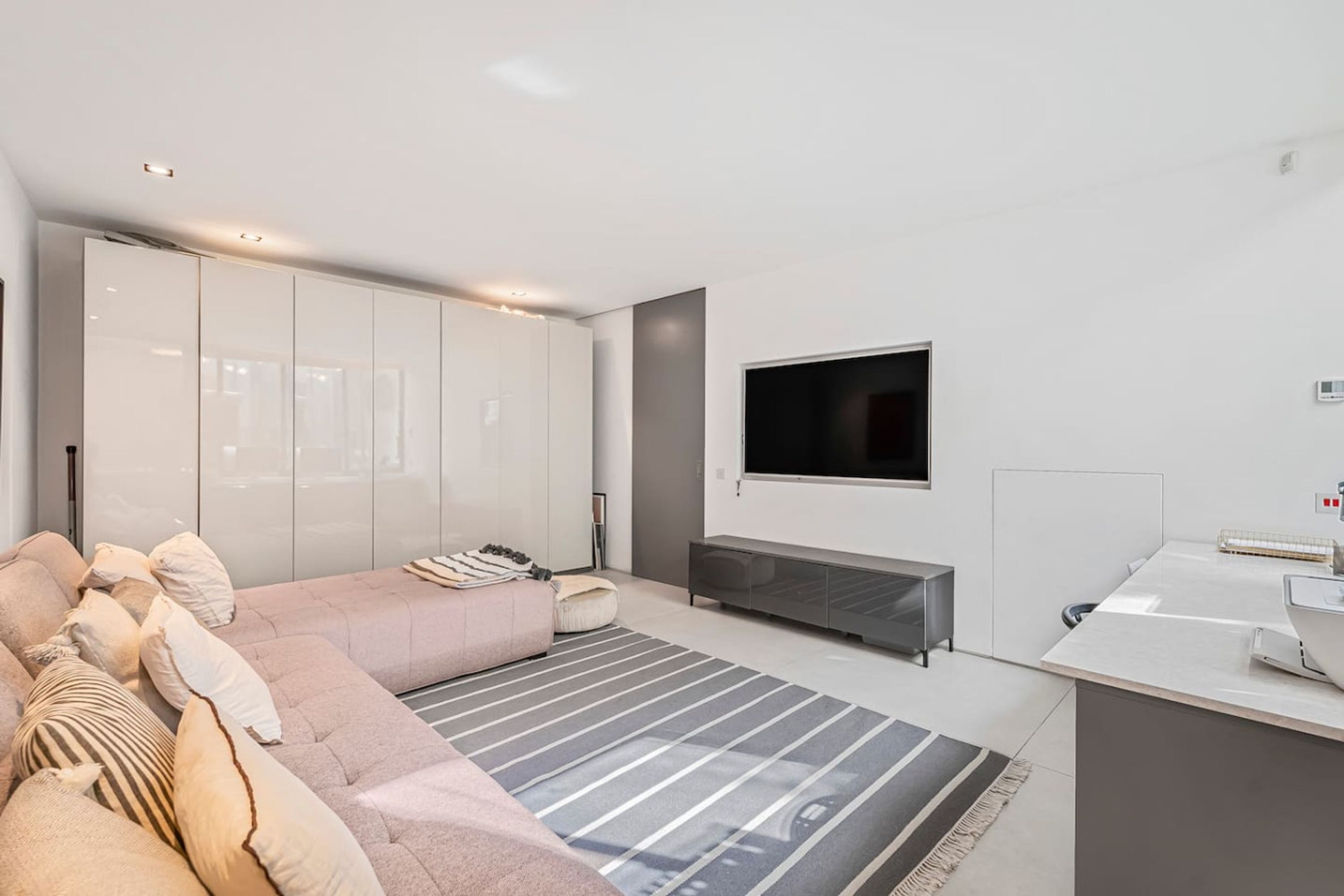 A modern living room with a sofa, a flat-screen TV mounted on the wall, and a minimalist design.