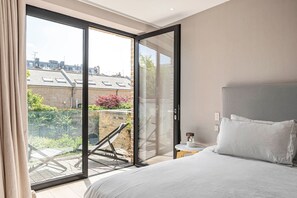 Une chambre dotée d’une grande porte-fenêtre coulissante donnant sur un balcon avec une chaise et une table.