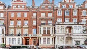 A row of red brick townhouses with bay windows, a black car parked in front, and a clear blue sky. - Cadogan Square Penthouse (London)