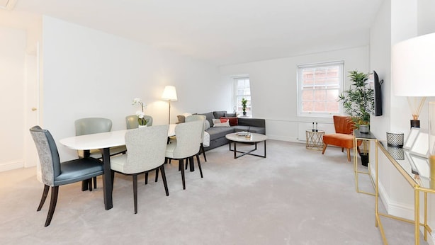 A modern living room with a dining area, a sofa, and a TV mounted on the wall. - Cadogan Square Penthouse (London)