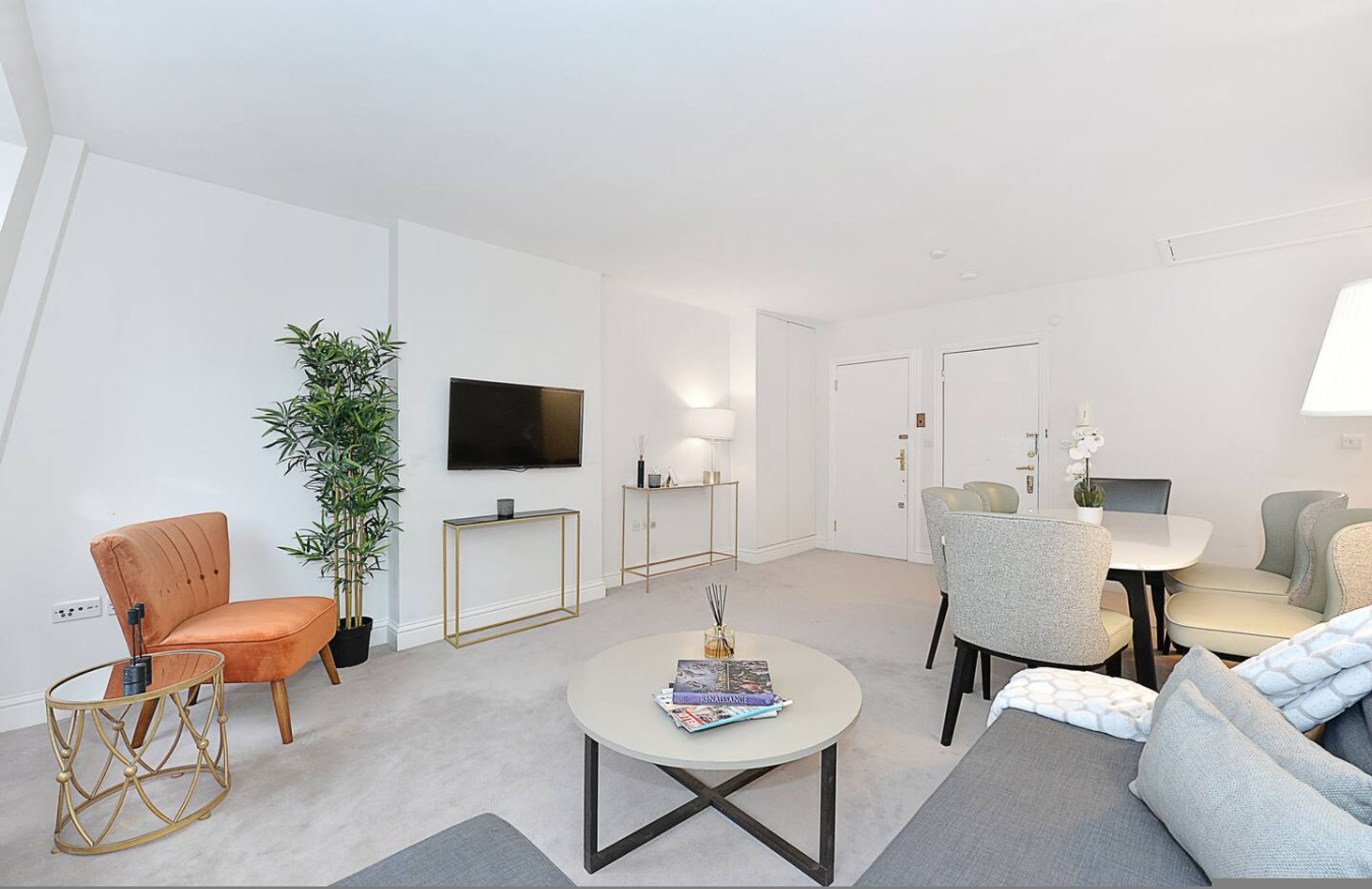 Uma sala de estar moderna com sofá, poltrona, mesa de centro e TV na parede.