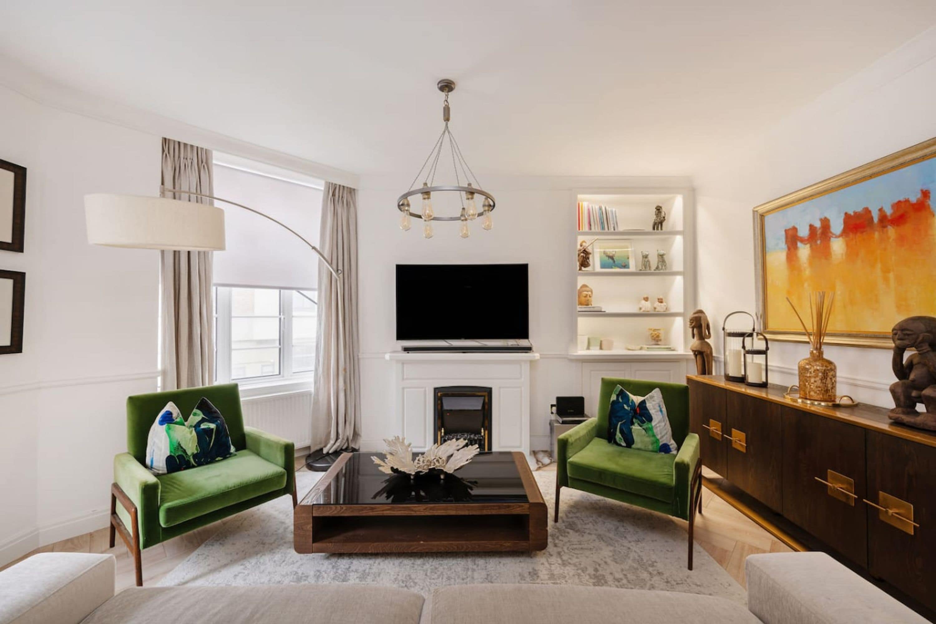 Een moderne woonkamer met een open haard, groene fauteuils, een bijzettafeltje en een groot schilderij.