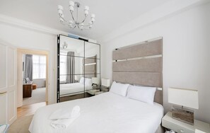 Ein modernes Hotelzimmer mit einem großen Bett, einem Schminktisch, einem Nachttisch mit Lampe und einem Kronleuchter.