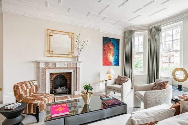 A living room with a fireplace, a large abstract painting, and a view of the city through large windows. - Holland Park 4-bed Balcony AC Lift Step Free (London)