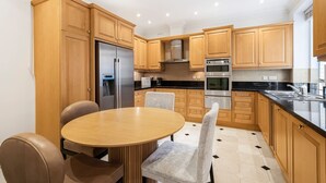 A modern kitchen with wooden cabinets, a stainless steel refrigerator, a built-in oven, and a black countertop. - Luxury 3BR Mayfair Apartment Near Green Park (London)
