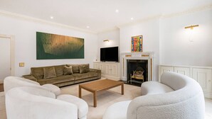 A living room with a sofa, armchairs, a coffee table, a fireplace, and artwork on the walls. - Luxury 3BR Mayfair Apartment Near Green Park (London)