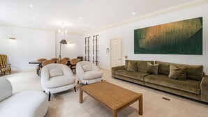 A modern living room with a sofa, armchairs, a coffee table, and a dining area with chairs and a table. - Luxury 3BR Mayfair Apartment Near Green Park (London)