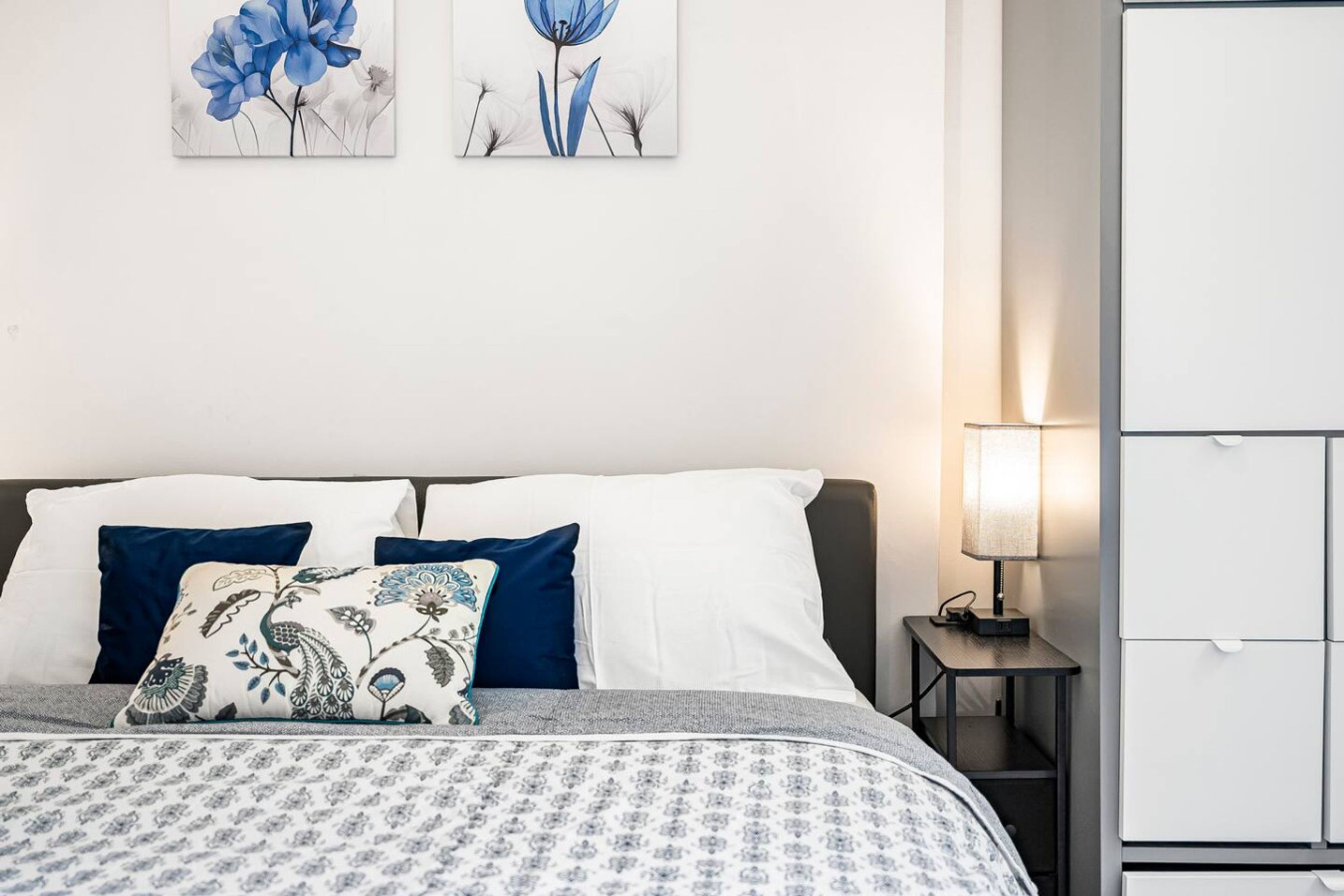 Una cama bien hecha con ropa de cama estampada, una mesita de noche con lámpara y un armario blanco.