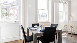 Un coin repas avec une table dressée pour quatre personnes, de grandes fenêtres et une vue sur les bâtiments environnants.
