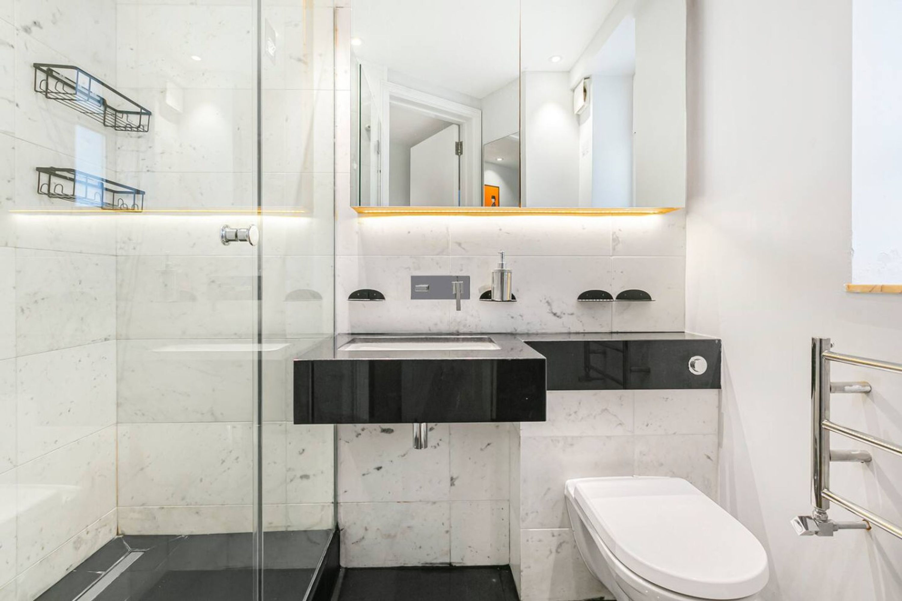 Un baño moderno con cabina de ducha de vidrio, lavamanos negro y váter blanco.