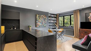 Eine moderne Küche mit einer Marmorinsel, eine Essecke mit einem runden Tisch und ein Wohnzimmer mit einer Couch und einem Fernseher.