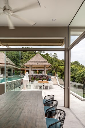 A modern outdoor dining area with a wooden table and chairs, a thatched-roof structure, and a pool in the background. - Koh Samui Villa in ko Samui (Koh Samui)