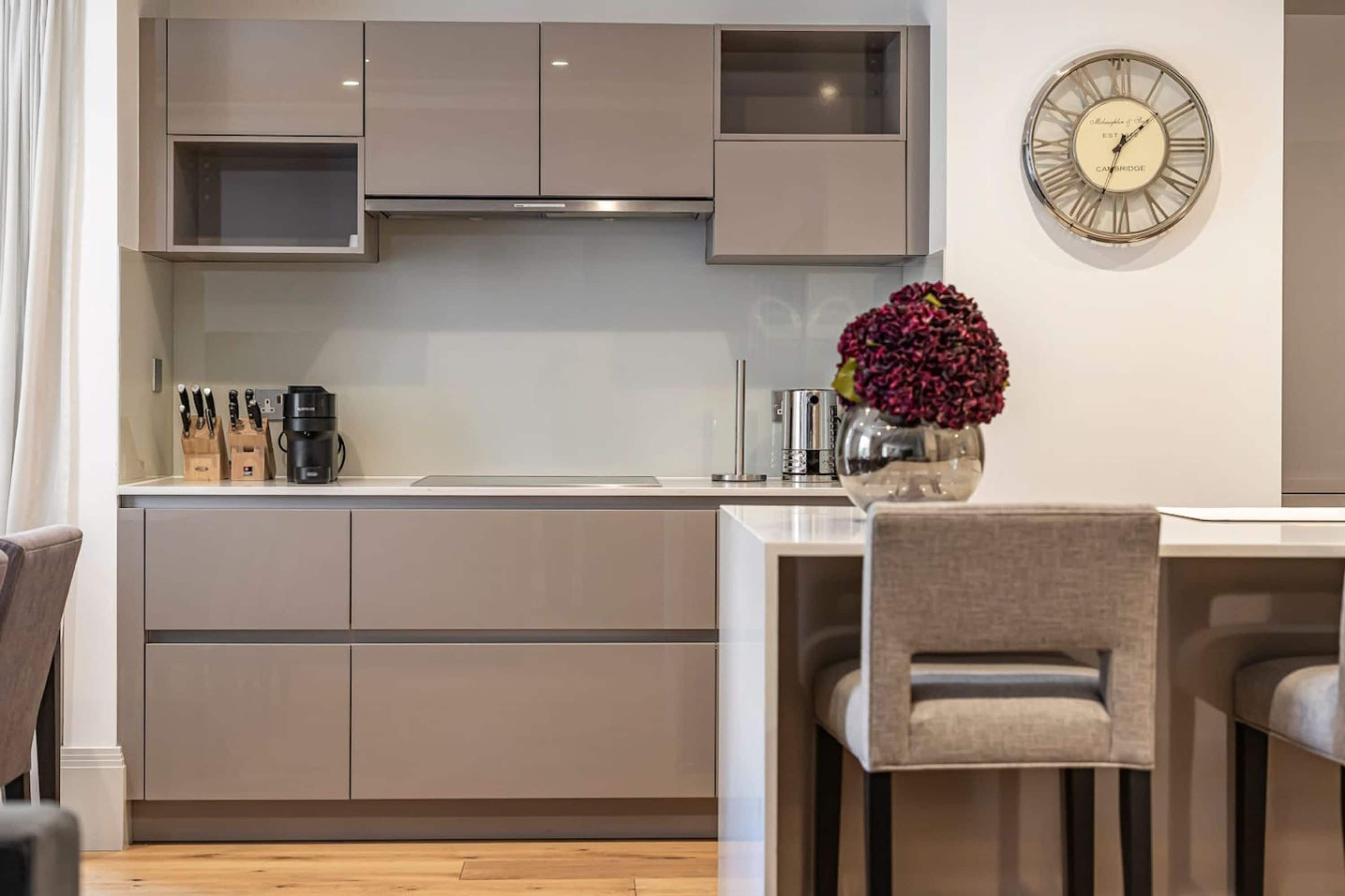 A modern kitchen with grey cabinets, a stainless steel range hood, and a wall-mounted clock.