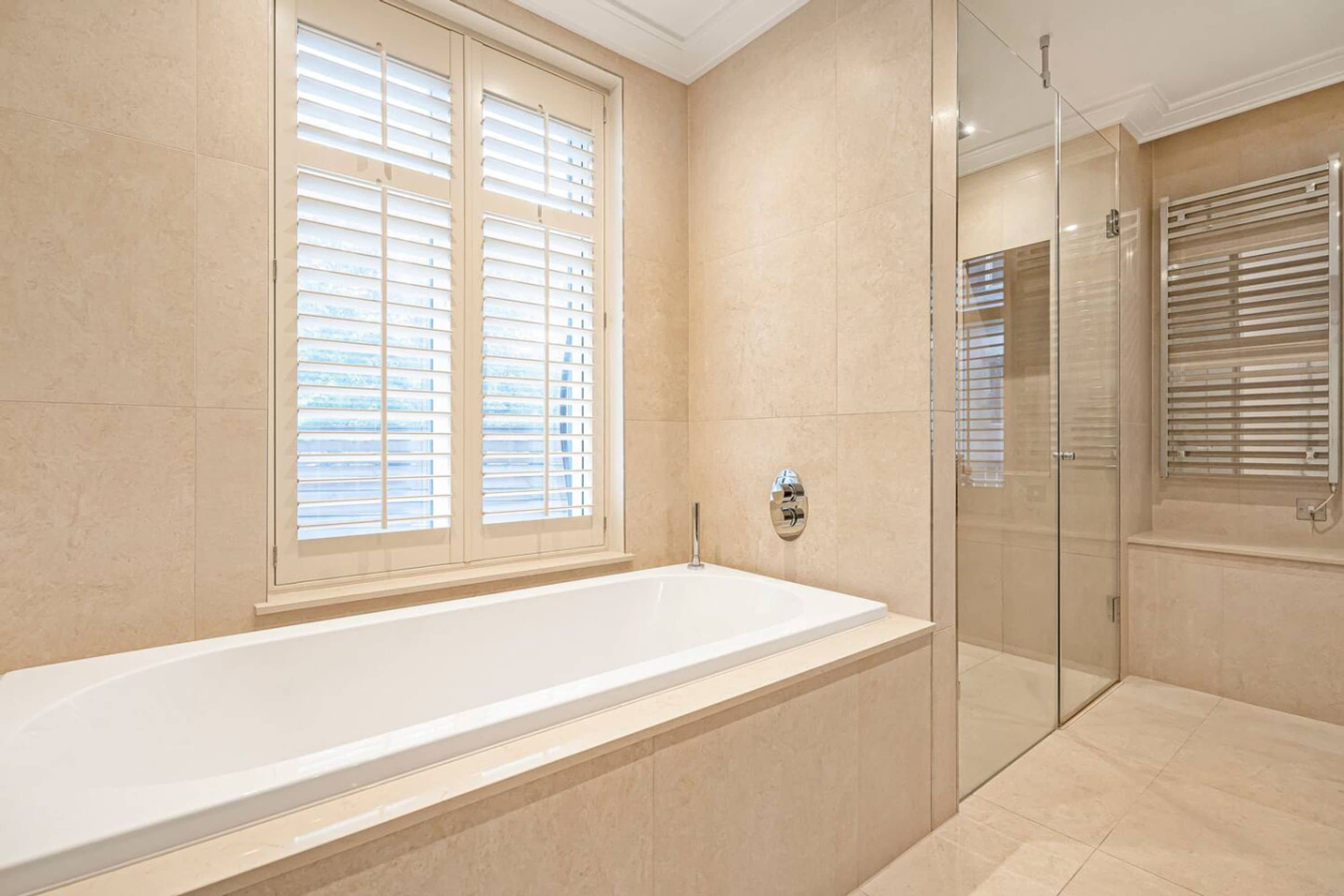 Een moderne badkamer met een groot bad, een douchecabine van glas en een raam met zonwering.