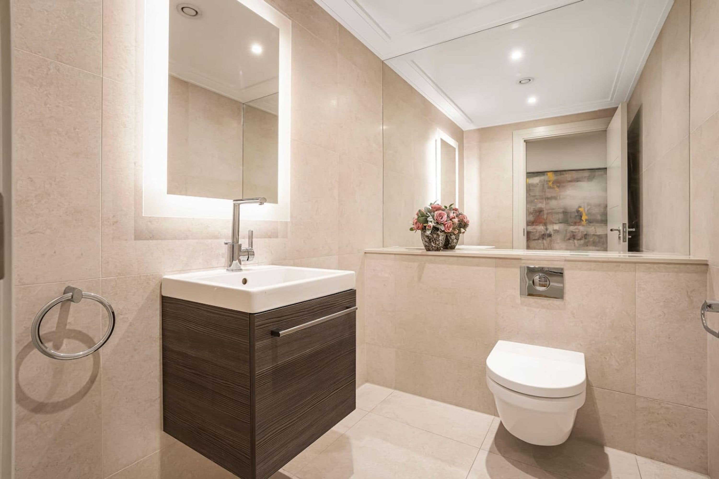 A modern bathroom with a large mirror, a sink, a toilet, and a decorative vase.
