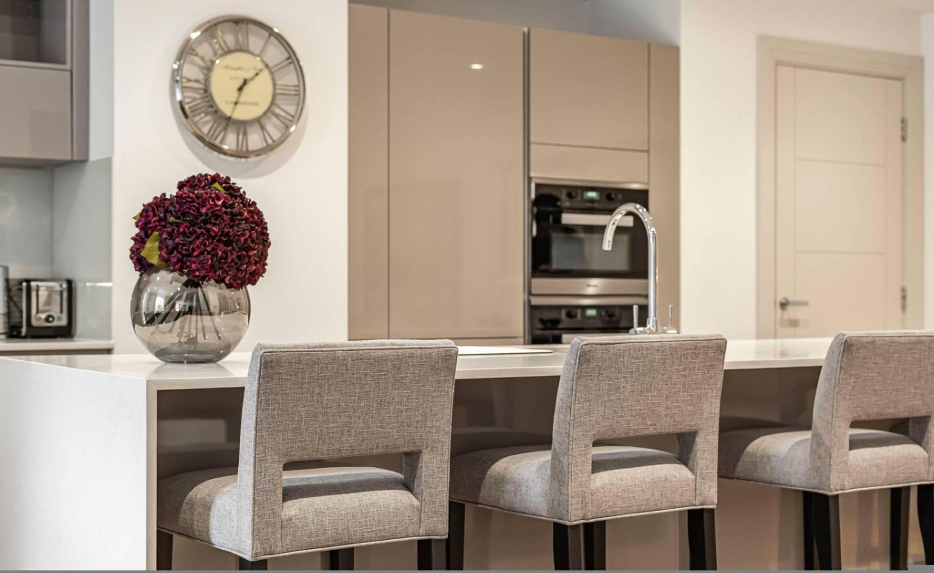 A modern kitchen with a central island, stainless steel appliances, and a clock on the wall.