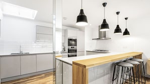 Una cocina moderna con armarios blancos, encimera de madera y lámparas colgantes negras.