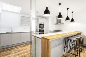 Eine moderne Küche mit weißen Schränken, einer Holz Arbeitsplatte und schwarzen Pendelleuchten.