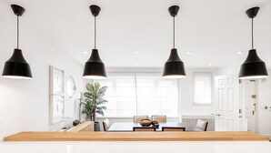 Una cocina moderna con una isla central, iluminación colgante y un comedor con sillas y una mesa.