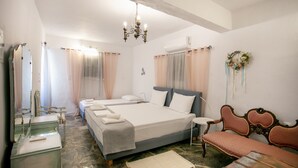 Ein Hotelzimmer mit einem großen Bett, zwei kleineren Betten, einem Frisiertisch mit Spiegel, einer Holzbank und einer Chandelier.