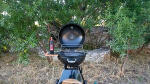 Ein tragbarer Grill mit geöffnetem Deckel, eine Weinflasche und ein Holzstoß.