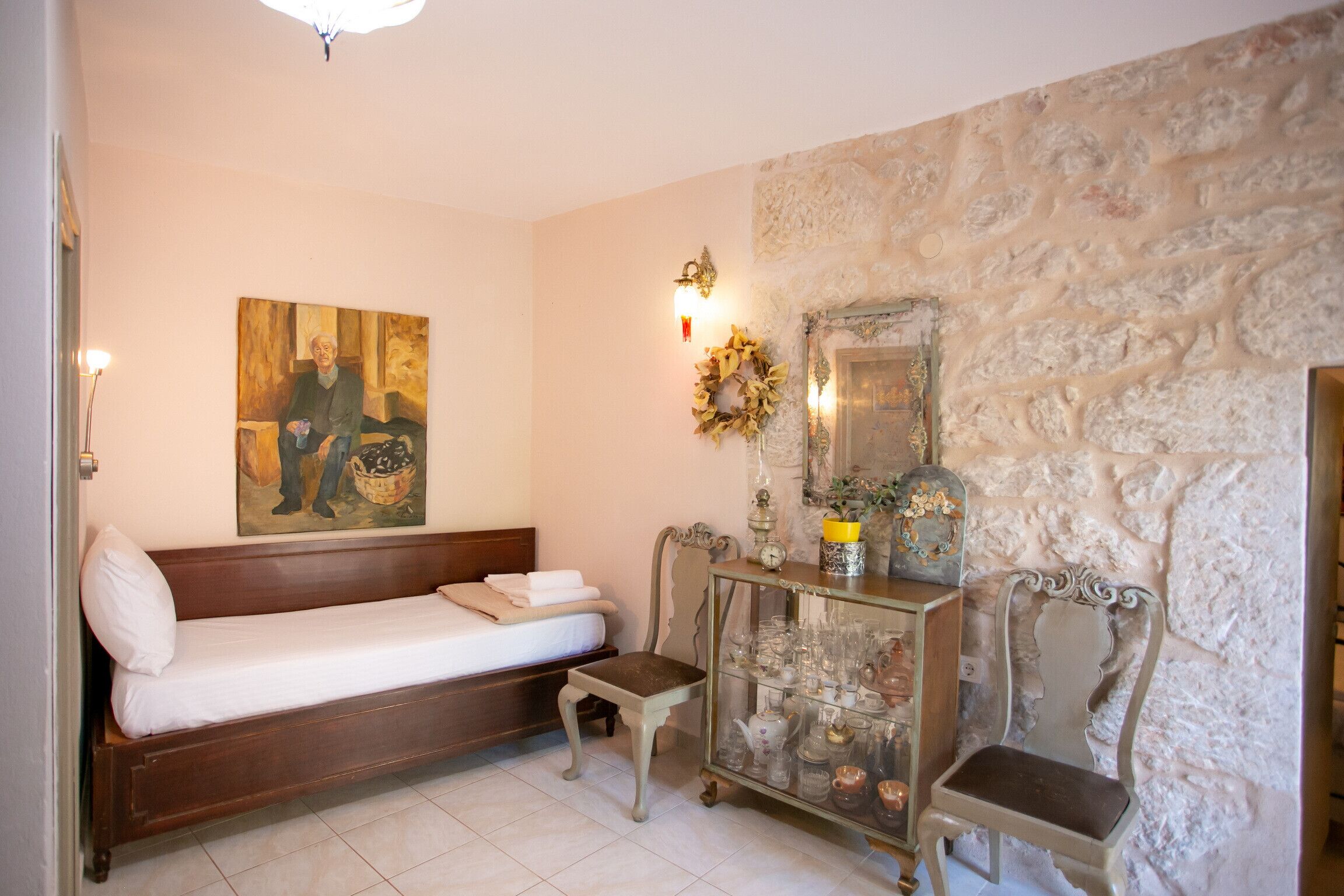 Una habitación con una cama de madera, una pequeña mesa con cristalería, una pared de piedra y un cuadro colgado.