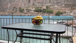 A table with a fruit bowl on a balcony overlooking a coastal area with rocky cliffs and buildings. - Gerolimin Blue (East Mani)