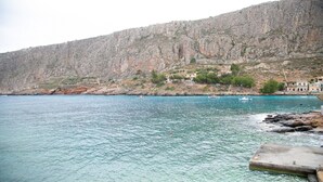 A coastal area with rocky cliffs and a clear blue sea. There are buildings on the cliffs and a dock extending into the water. - Gerolimin Blue (East Mani)