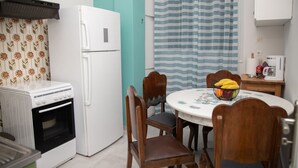 A compact kitchen with a white refrigerator, a stove, and a microwave. There is a dining table with chairs and a bowl of fruit. - Gerolimin Blue (East Mani)
