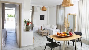 Una sala de estar moderna con comedor, muebles blancos, un espejo grande y un frutero sobre la mesa.