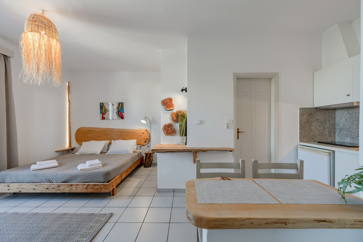 Un dormitorio moderno con una cama de madera, una mesita de noche, una lámpara colgante y una pequeña zona de escritorio con una silla.