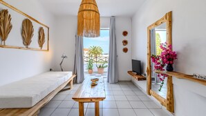 Una habitación con cama, una mesa de madera, un televisor y un balcón con plantas.