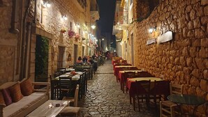 Een smalle straat met keien, omzoomd door stenen gebouwen, met terrasjes en verlicht door lantaarns.