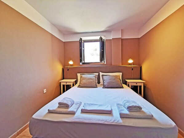 Un dormitorio con una cama, dos mesitas de noche, un ventanal y dos lámparas de pared.
