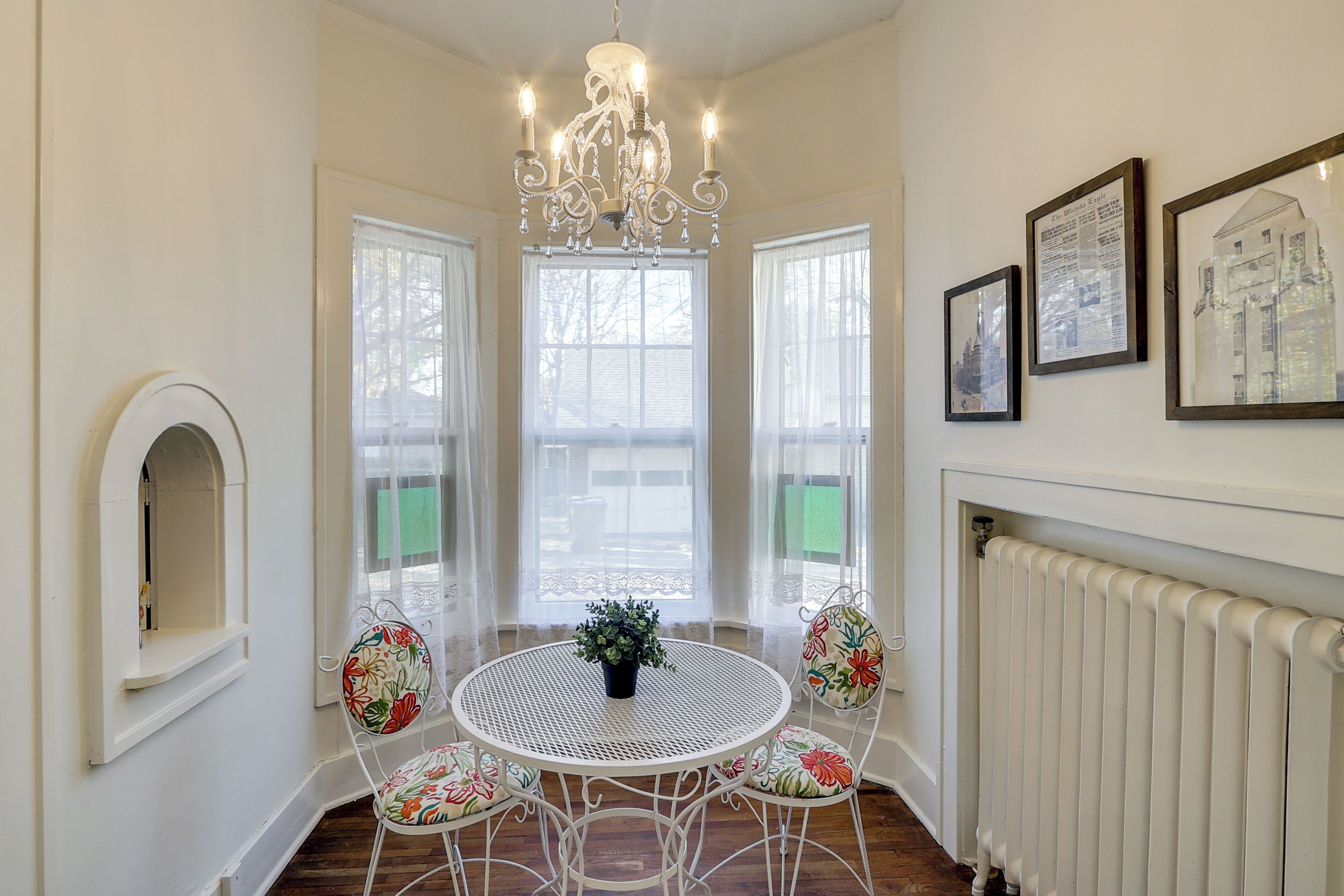 A dining area with a round table, chairs, a chandelier, and framed pictures on the wall.