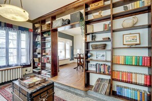 A room with wooden bookshelves filled with books and decorative items, a vintage trunk, and a globe on a table.