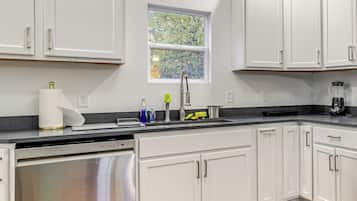 A modern kitchen with white cabinets, a stainless steel dishwasher, a sink with a faucet, and a window above the sink.