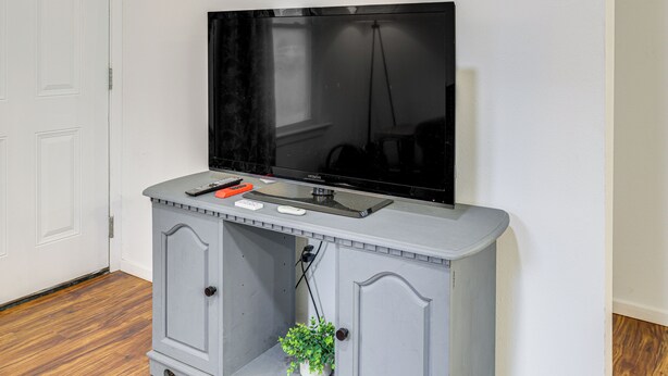 Ein Fernseher, der an einem grauen Schrank befestigt ist, mit Fernbedienung und Maus darauf.