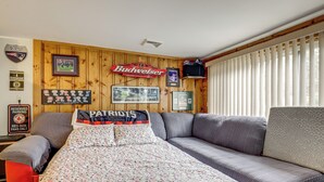 Une pièce avec un mur en bois, un canapé, un lit recouvert d’une courtepointe à motifs floraux et une enseigne sur laquelle on peut lire « Budweiser ».