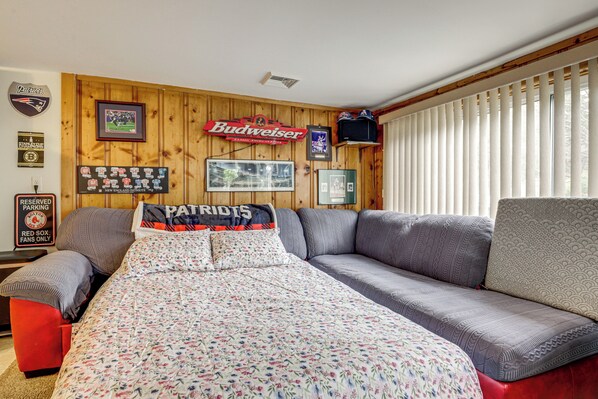 Una habitación con pared de madera, un sofá, una cama con colcha estampada y un cartel que dice "Budweiser".