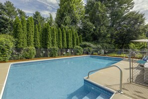 A rectangular swimming pool with a metal safety railing, surrounded by a chain-link fence and lush greenery. - Hike & Explore Western Mass: Peaceful Studio (Palmer)