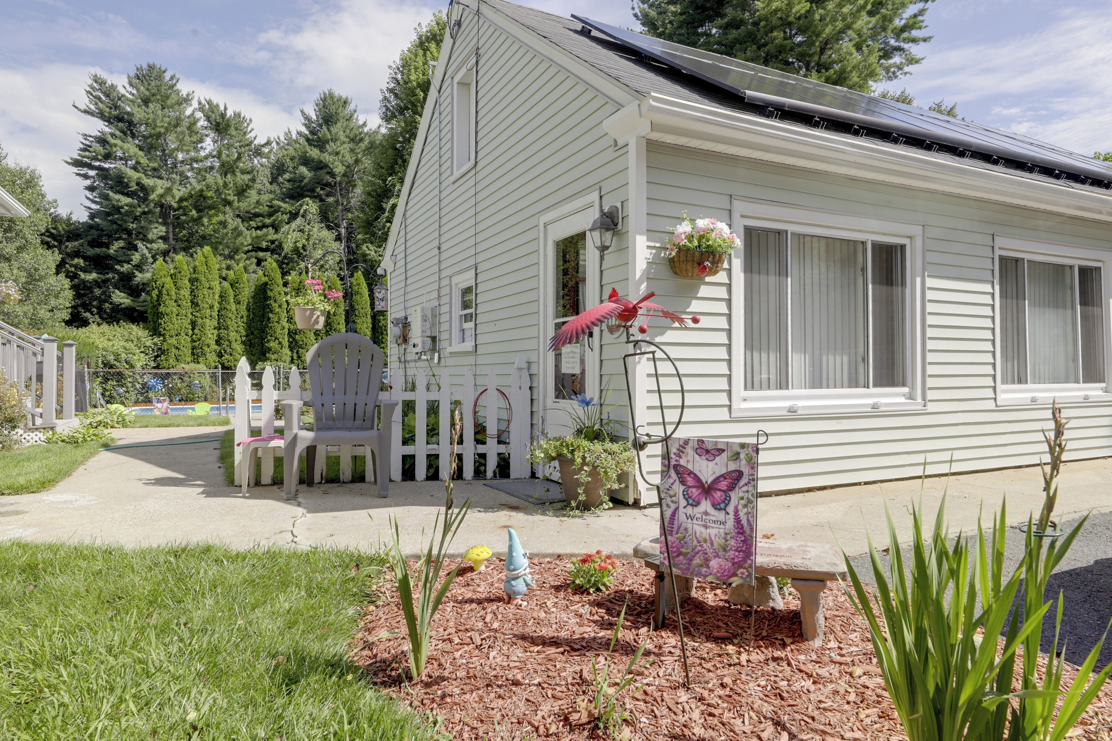 A house with a white exterior, a front porch with a bench, and a small garden area with mulch and plants.