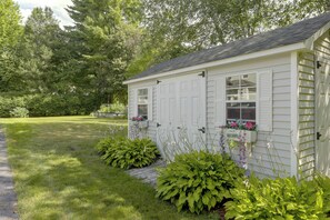 A small white building with a sloped roof, a garage door, and a window with a welcome sign. - Hike & Explore Western Mass: Peaceful Studio (Palmer)