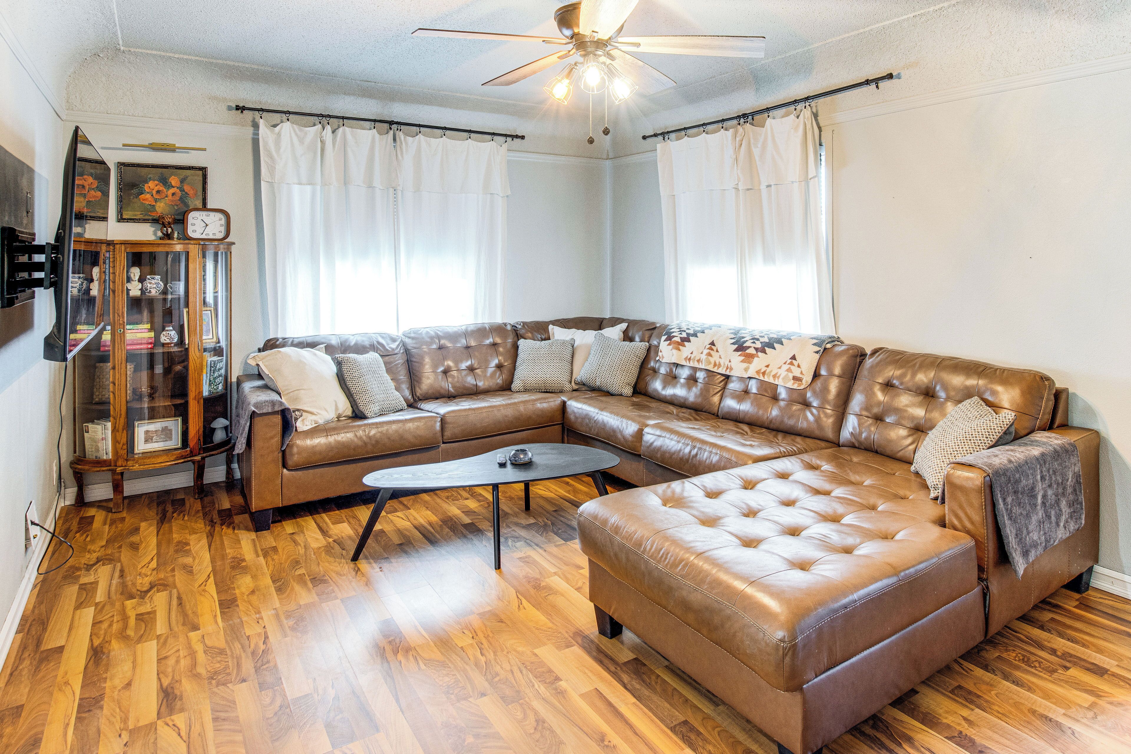 Una sala de estar con un sofá seccional de cuero marrón, una mesa de centro y un mueble de madera con puertas de vidrio.
